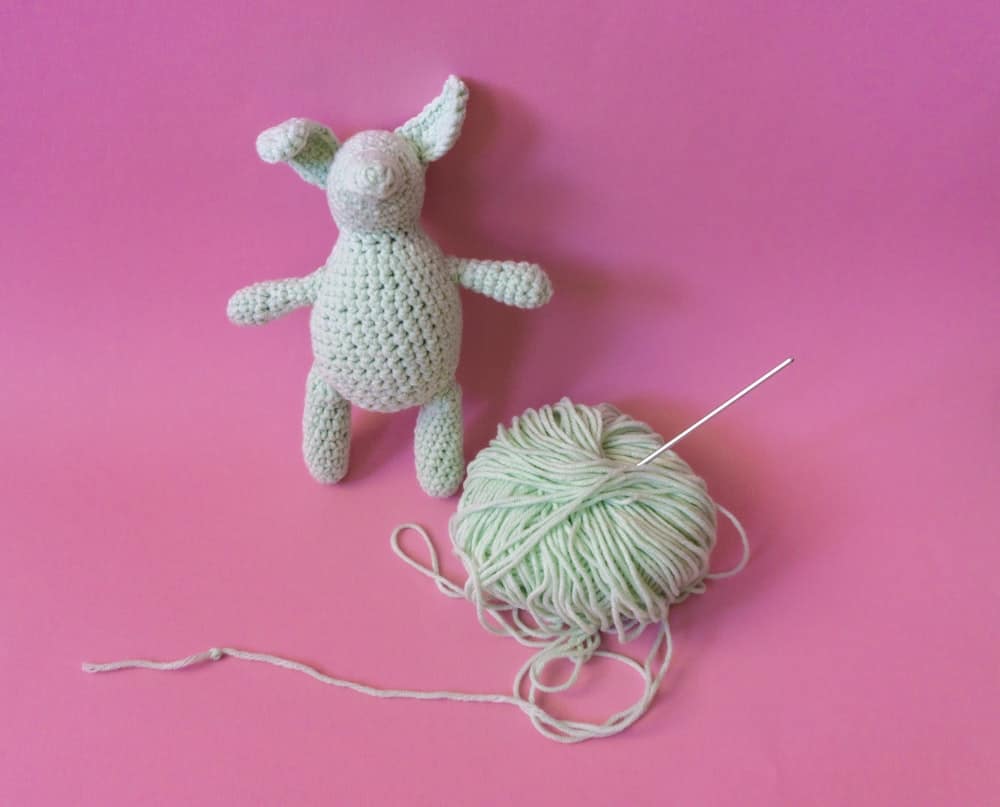 A mint green crocheted amigurumi bunny beside a ball of yarn