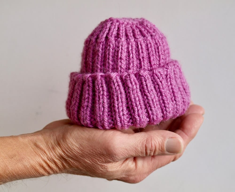 A hand holding a small pink knit baby cap